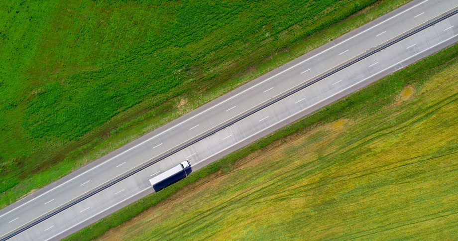 Ein LKW auf einer Zweispurigen Landstraße umgeben von Feldern, Sicht von Oben