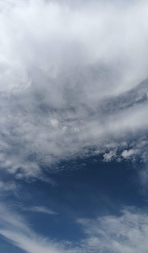 Ein Himmel voller dicker, wirbelnder Wolken in verschiedenen Grau- und Weißtönen, deren Bewegung an die Präzision und Koordination einer nahtlosen Kooperation erinnert, während Flecken eines tiefblauen Himmels durchscheinen. - NG.network