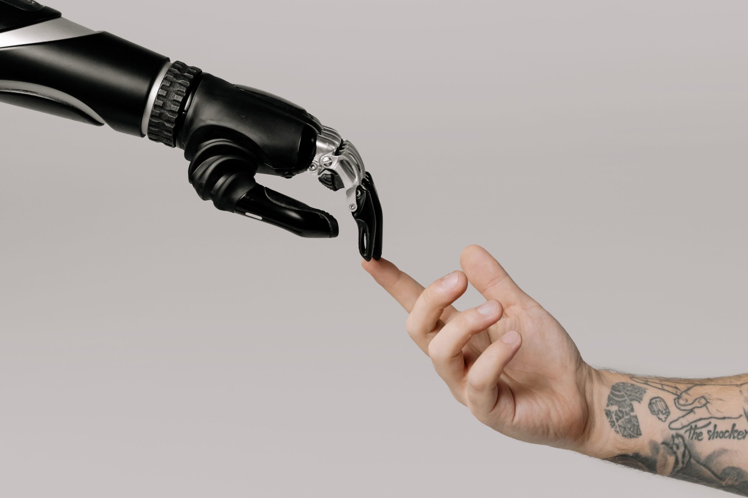 Foto einer Roboterhand und einer Menschenhand, die sich mit jeweils einer Fingerspitze mittig im Bild berühren.